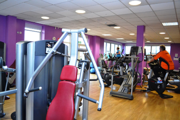Ein Fitnessstudio mit verschiedenen Geräten und einigen Menschen, die trainieren, mit einer Decke und Lampen an der Spitze.