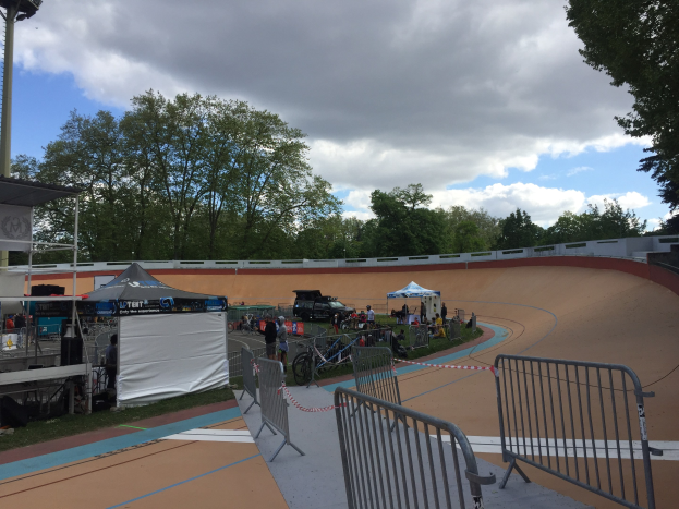 Gruppe von Radfahrern auf einer Schotterstrecke bei den UCI BMX-Weltmeisterschaften 2018, mit Zuschauern, Zelten und Fahrzeugen im Hintergrund.