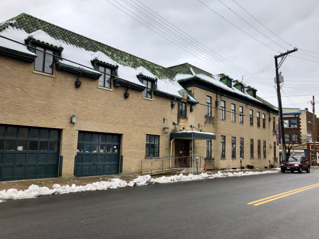 Großes Ziegelgebäude mit grüner Dachfläche an einer Straßenkreuzung, als ehemalige St. Louis-Feuerwache bezeichnet, umgeben von Fahrzeugen, Schnee, Strommasten, Bäumen und einem bewölkten Himmel.