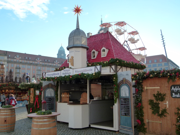 Ein kleines Gebäude mit einem roten Dach und einem Riesenrad davor, umgeben von Menschen und Festschmuck.