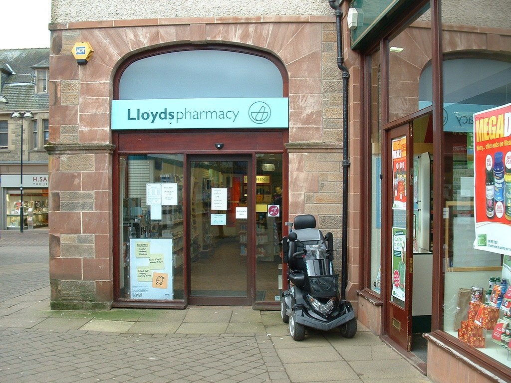 Apothekenladen mit einem Fahrzeug vorne und einem Gebäude in der linken Ecke.