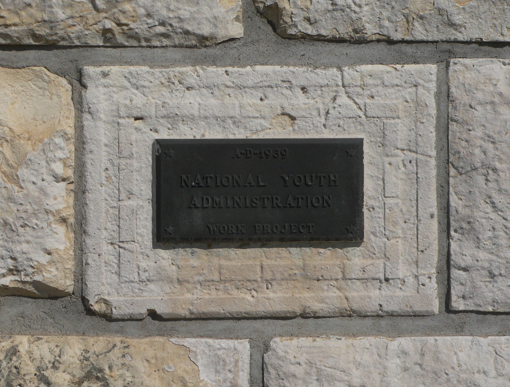 Steinwand mit einem rechteckigen Schild, auf dem in fetten weißen Buchstaben 'Nationaler Jugenddienst' steht.