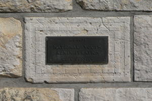 Steinwand mit einem rechteckigen Schild, auf dem in fetten weißen Buchstaben 'Nationaler Jugenddienst' steht.