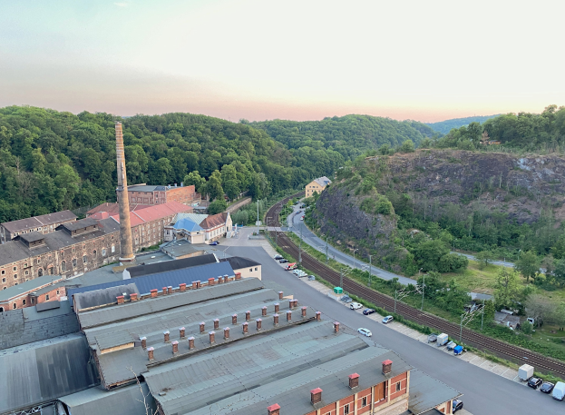 Luftaufnahme einer Stadt mit dichtem Gebäudebestand, befahrenen Straßen, Strommasten, vereinzelten Bäumen, fernen Hügeln und einem bewölkten Himmel, die an ein Kohlebergbaugebiet erinnern.