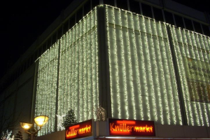 Ein festlich geschmücktes Gebäude in Berlin, Deutschland, mit Weihnachtslichtern, umgeben von Bäumen, Laternenmasten und Texttafeln, mit dem Himmel im Hintergrund.