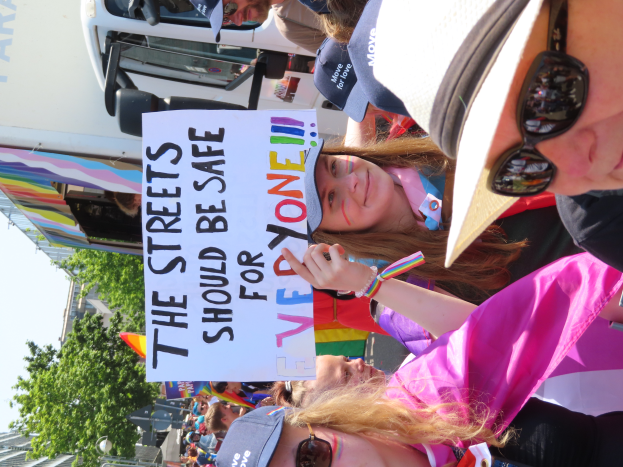 Eine Gruppe von Menschen steht vor einem Truck und hält ein Schild hoch, auf dem "Die Straßen sollten sicher sein" steht. Einige tragen Mützen und Schutzbrillen, andere halten Schilder. Im Hintergrund sind Bäume, Gebäude und ein klarer blauer Himmel zu sehen.
