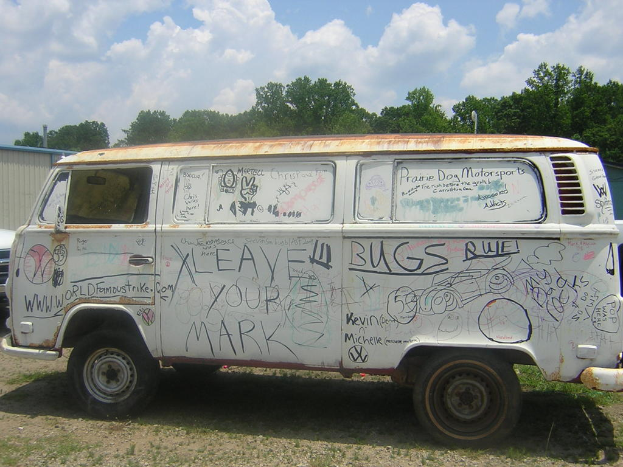 Ein besch√§digt aussehender Lieferwagen mit Bildern und Zitaten darauf, der vor einem waldigen Gebiet geparkt ist.