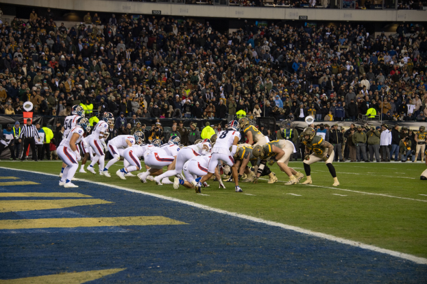 Fussballspieler in Sportkleidung und Helmen auf dem Boden liegend während eines Spiels in einem Stadion mit Zuschauern und Tafeln im Hintergrund.
