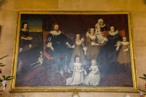 Gemälde einer Familie in einem Raum mit einem Weihnachtsbaum im Hintergrund, gerahmt und an einer Wand gehängt, mit zwei Foto Rahmen auf jeder Seite und dekorativen Gegenständen unten.