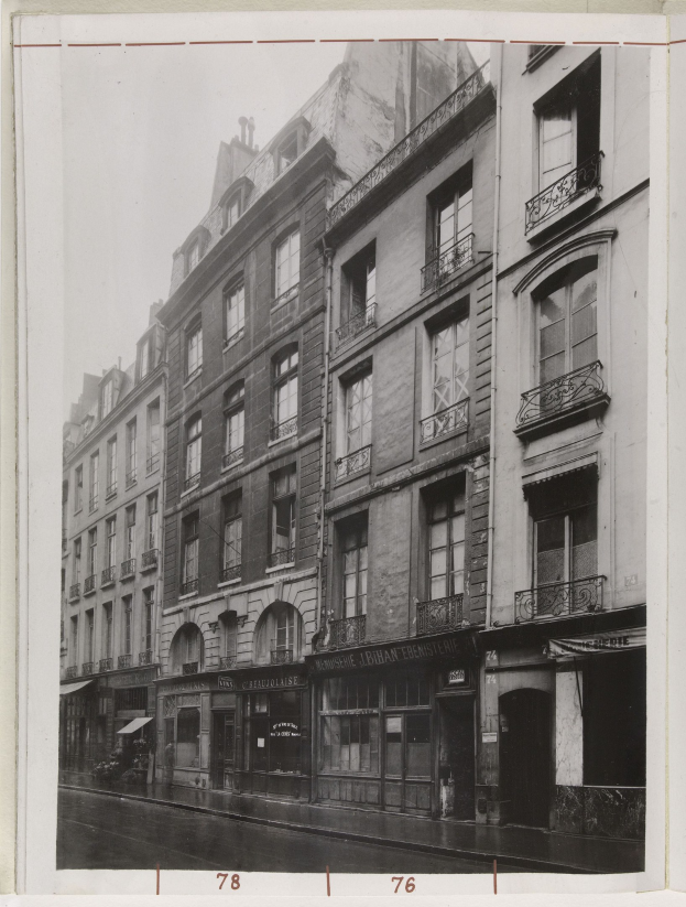 Schwarz-weiß-Foto einer Stadtstraße mit Gebäuden, Fenstern, Geländern, Namensschildern und einer Straße unten.
