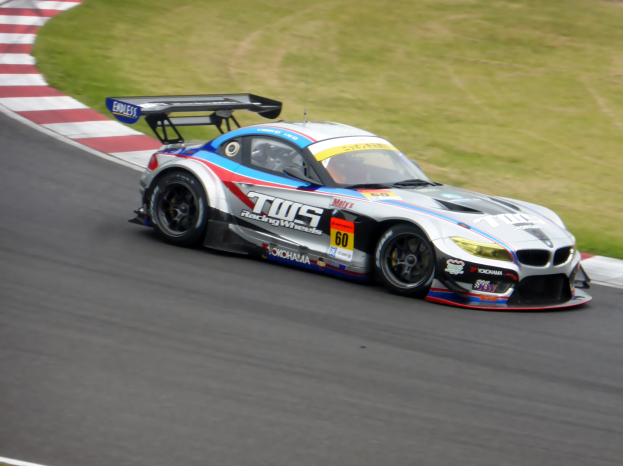 Ein BMW Z4 GT3 Rennwagen fährt auf einer Rennstrecke, mit Text und Zahlen auf dem Auto und Gras auf dem Boden.