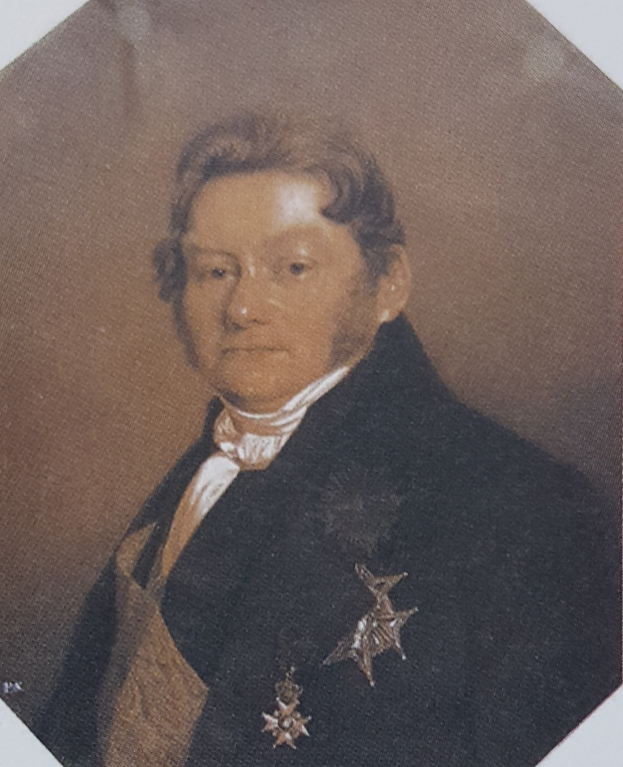 Ein Mann in einem schwarzen Anzug mit einer Stern auf der Brust, der formell mit einem ernsten Gesichtsausdruck und ordentlich frisiertem Haar steht.